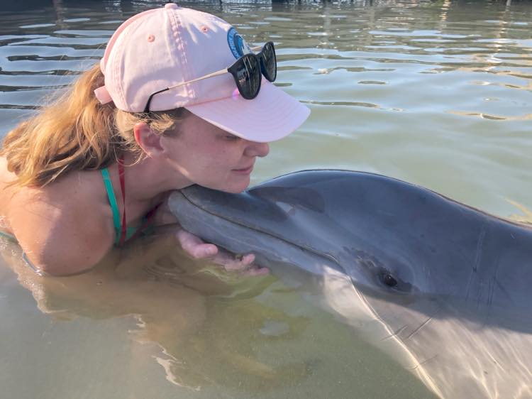 a woman in a pink hat is petting a dolphin