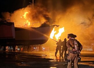 a group of fire fighters standing in front of a boat on fire