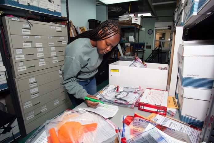 1 KWPD_APSMC_Milodjina_C Tedesco_1S0A0431 Large a woman standing in a room filled with boxes and papers