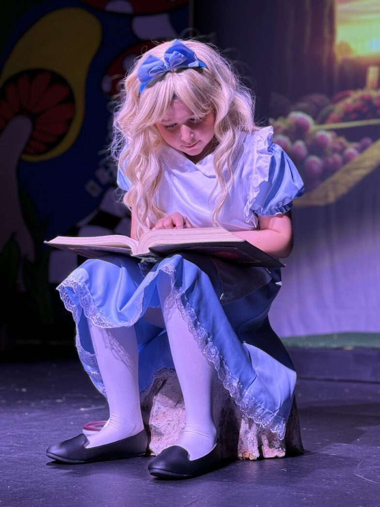 a young girl sitting on a stage reading a book