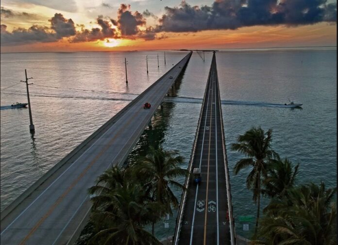 the sun sets over the ocean and a bridge