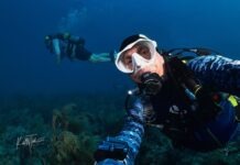 a man in a diving suit and goggles dives over a coral reef