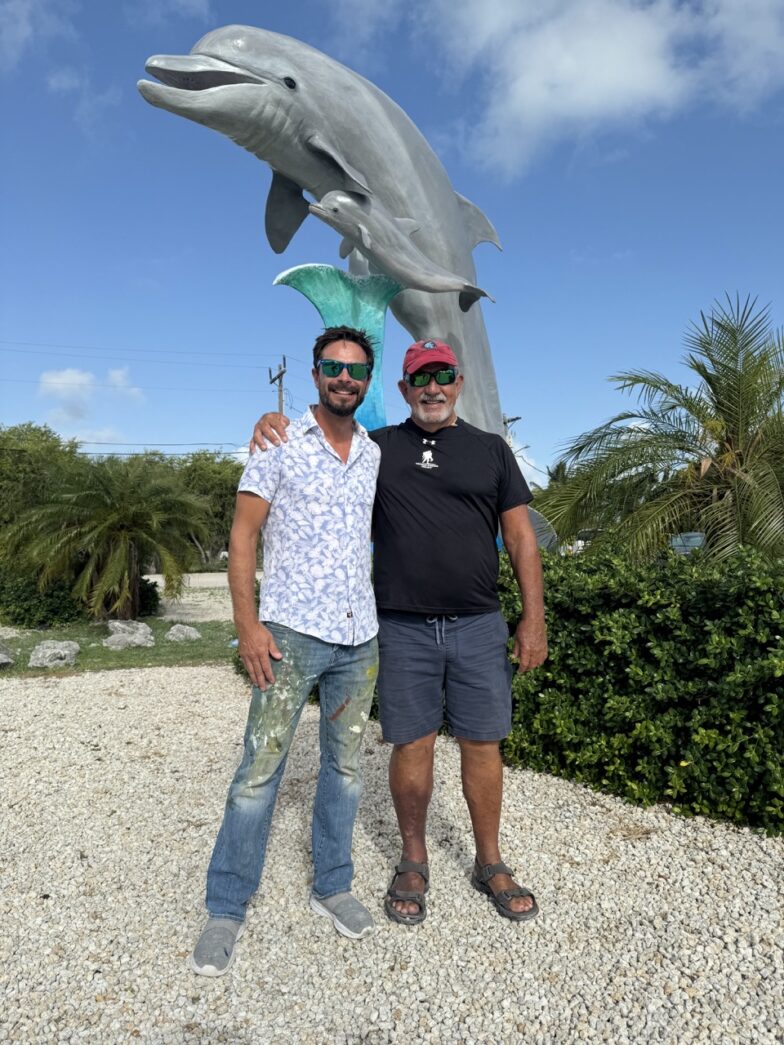 a couple of men standing next to a statue of a dolphin