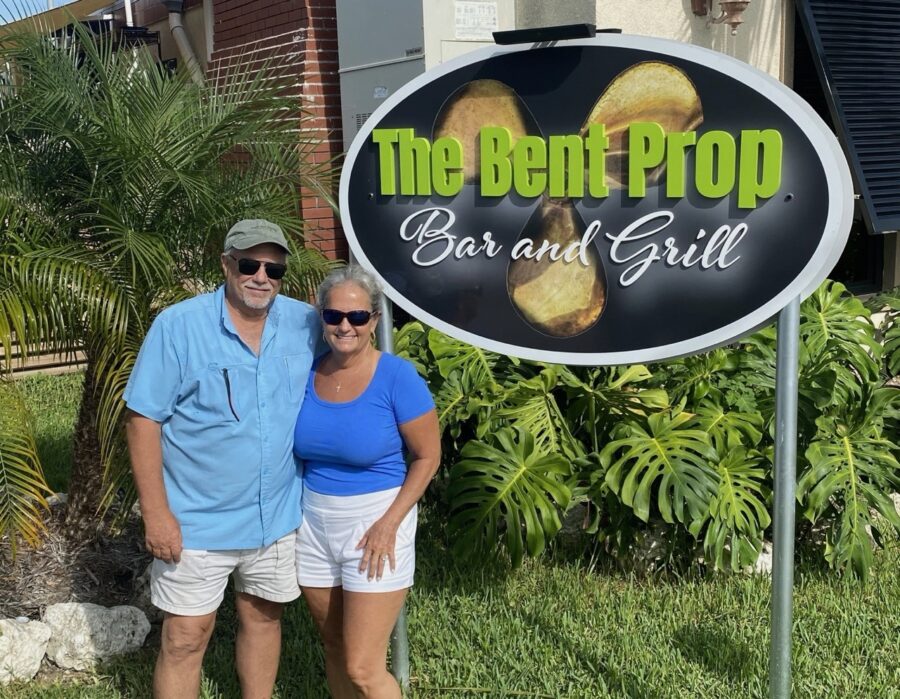 a man and woman standing in front of a bar and grill sign