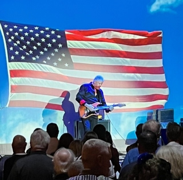 a man playing a guitar in front of an american flag