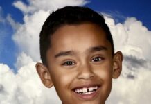a young boy smiling in front of a blue sky with clouds