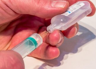 a hand holding a small plastic bottle with a needle in it