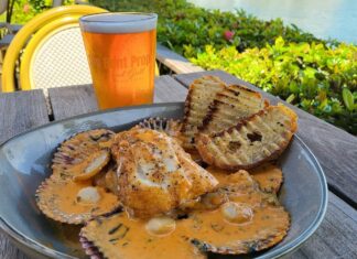 a bowl of food sitting on a table next to a glass of beer