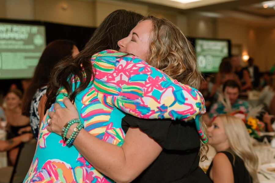 two women hugging each other in a room full of people