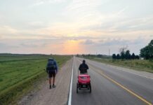 two people walking down a road with a baby in a stroller