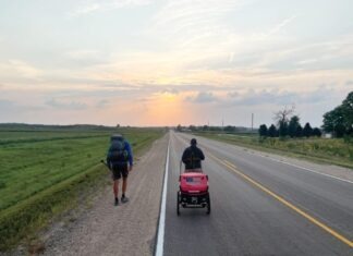 two people walking down a road with a baby in a stroller