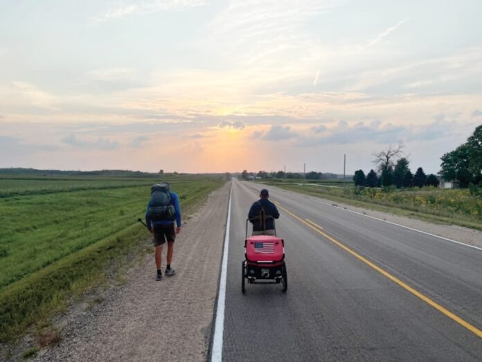 two people walking down a road with a baby in a stroller