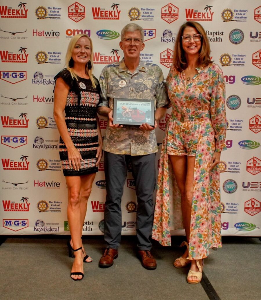 a man standing next to two women holding a plaque