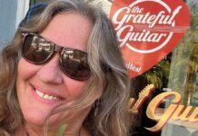 a woman wearing sunglasses and a flower in front of a guitar shop