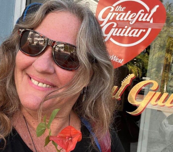 a woman wearing sunglasses and a flower in front of a guitar shop