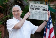 a man holding up a newspaper in front of an american flag