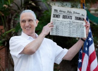 a man holding up a newspaper in front of an american flag