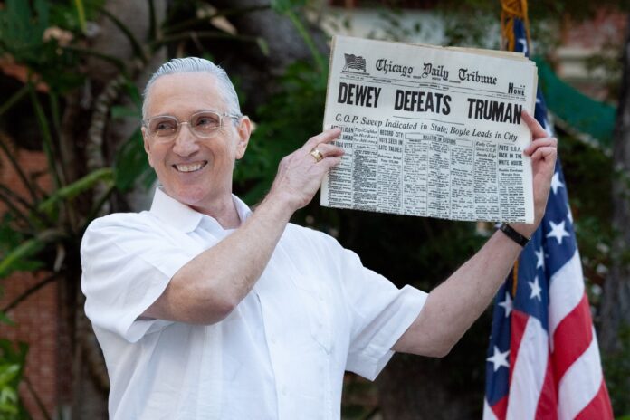 a man holding up a newspaper in front of an american flag