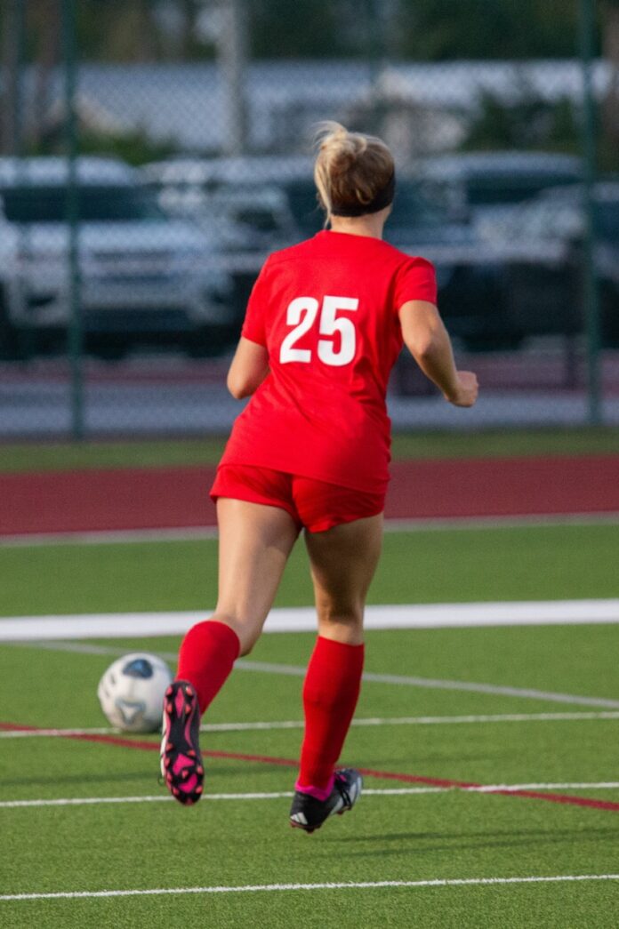 a woman in a red uniform kicking a soccer ball