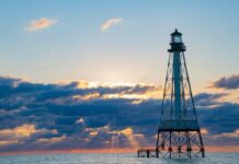 a lighthouse in the middle of the ocean at sunset