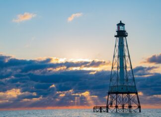 a lighthouse in the middle of the ocean at sunset