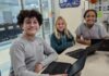 a group of young people sitting at a table with laptops