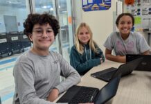 a group of young people sitting at a table with laptops