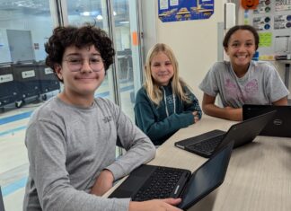 a group of young people sitting at a table with laptops