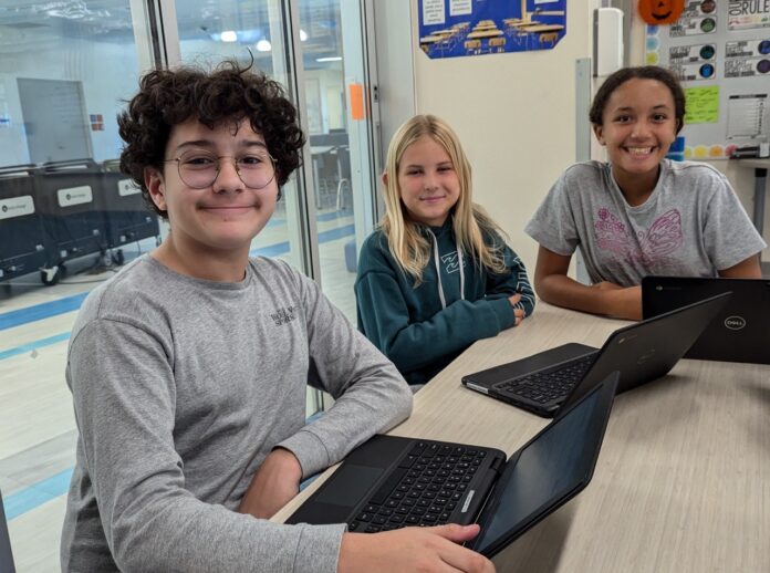 a group of young people sitting at a table with laptops