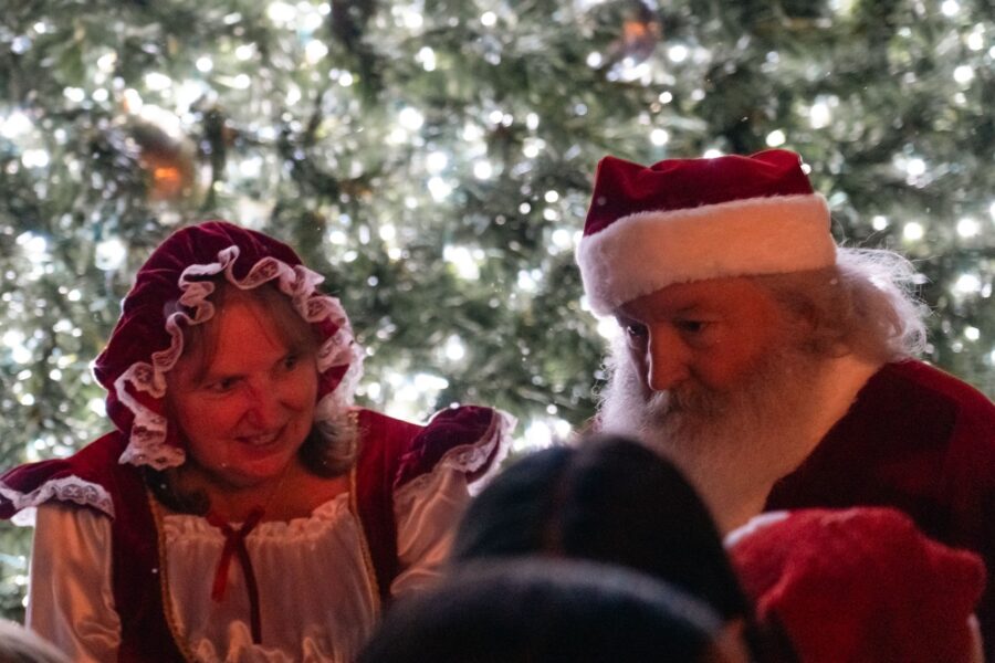 a man and a woman dressed as santa claus in front of a christmas tree