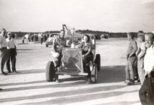 a black and white photo of people standing around a car