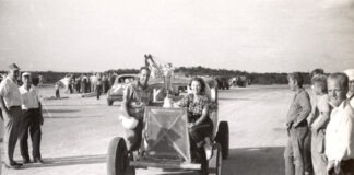 a black and white photo of people standing around a car