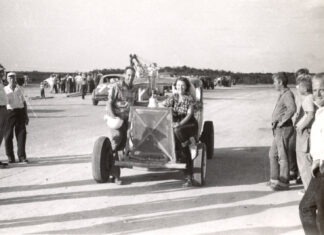 a black and white photo of people standing around a car