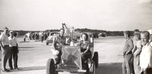 a black and white photo of people standing around a car
