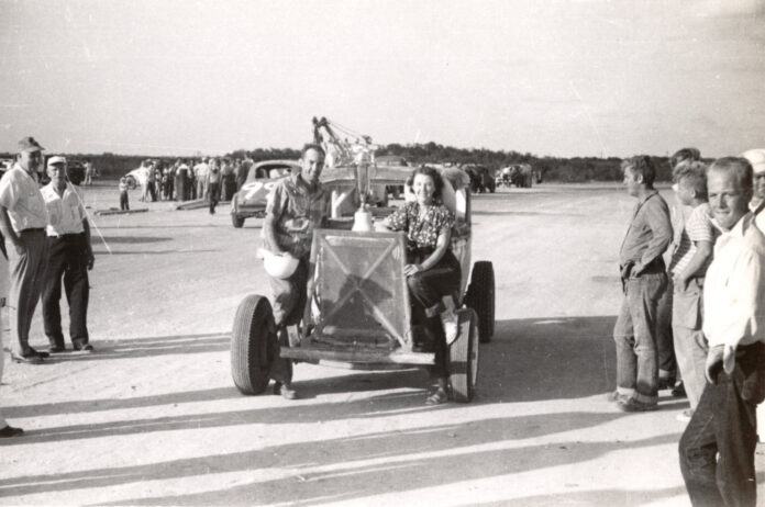 a black and white photo of people standing around a car