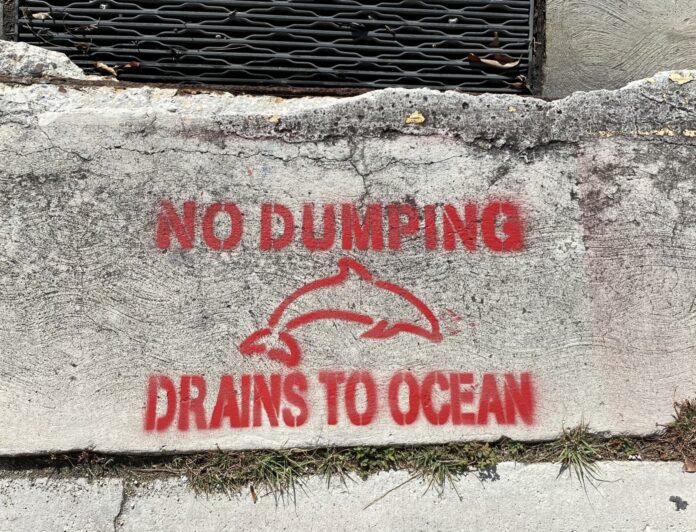 a sign on a concrete wall that says no dumping drains to ocean