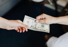 Two people exchanging a ten dollar bill in a close-up hand-to-hand transaction.