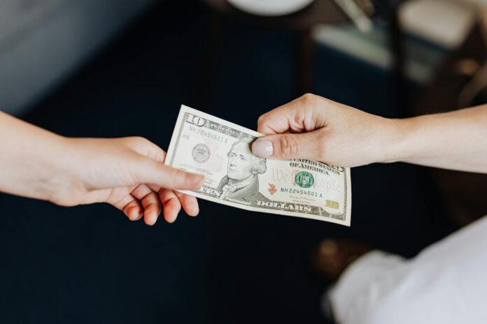 Two people exchanging a ten dollar bill in a close-up hand-to-hand transaction.