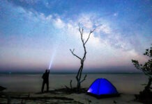 a man standing next to a blue tent under a night sky