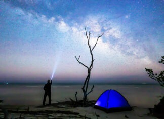 a man standing next to a blue tent under a night sky