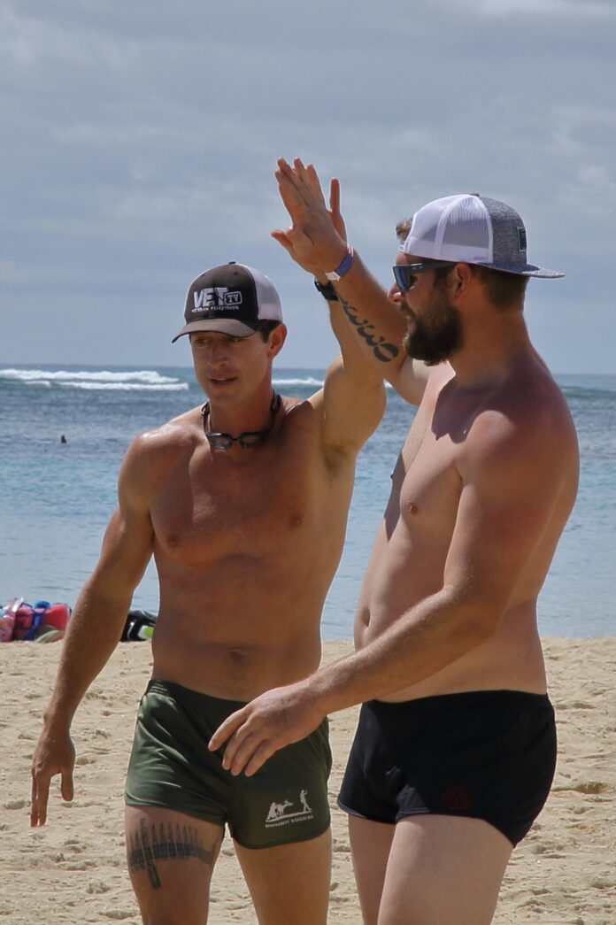 a couple of men standing on top of a sandy beach