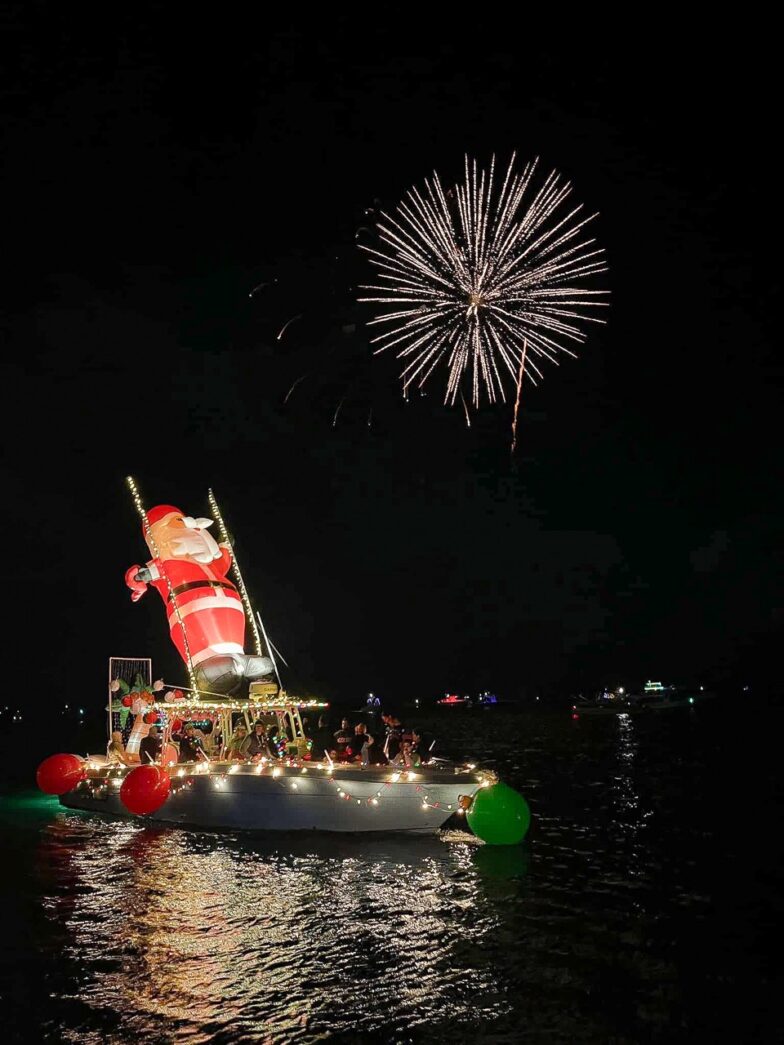 a boat with a flag on it floating in the water with fireworks in the sky