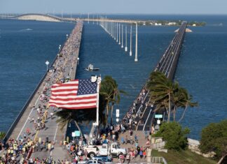 a crowd of people walking across a bridge next to the ocean