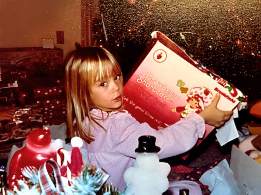 a little girl holding a christmas book in front of a window