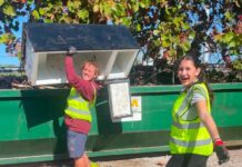 a couple of women standing next to a green dumpster