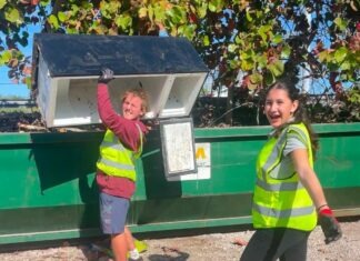 a couple of women standing next to a green dumpster