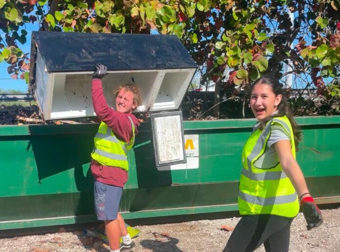 a couple of women standing next to a green dumpster