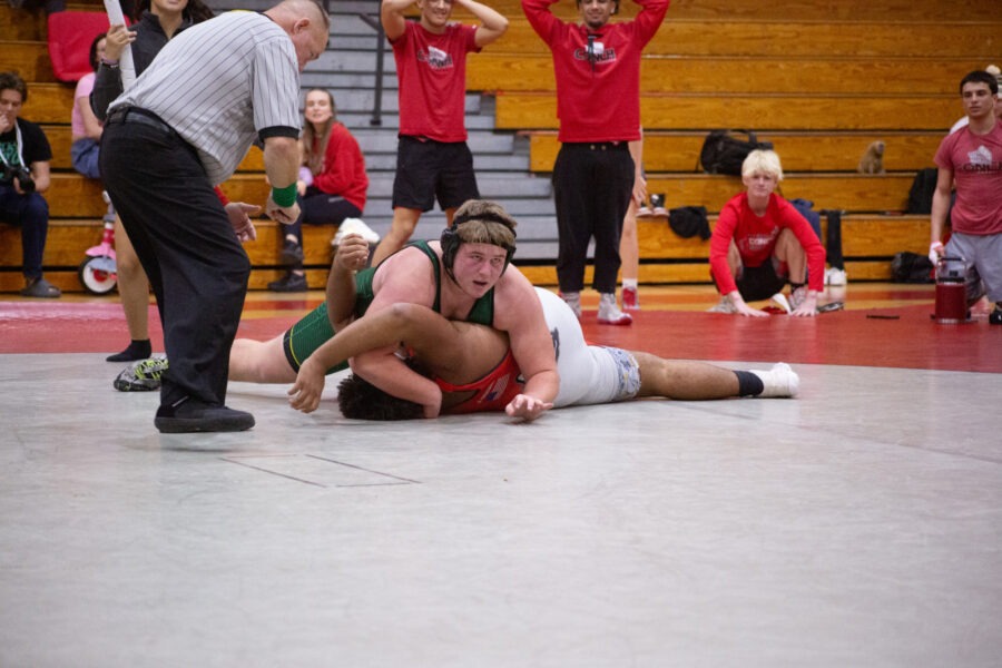 a wrestling match in progress with the referee looking on