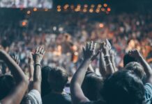 Energetic crowd at a live concert with hands raised and bright lights.