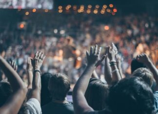 Energetic crowd at a live concert with hands raised and bright lights.